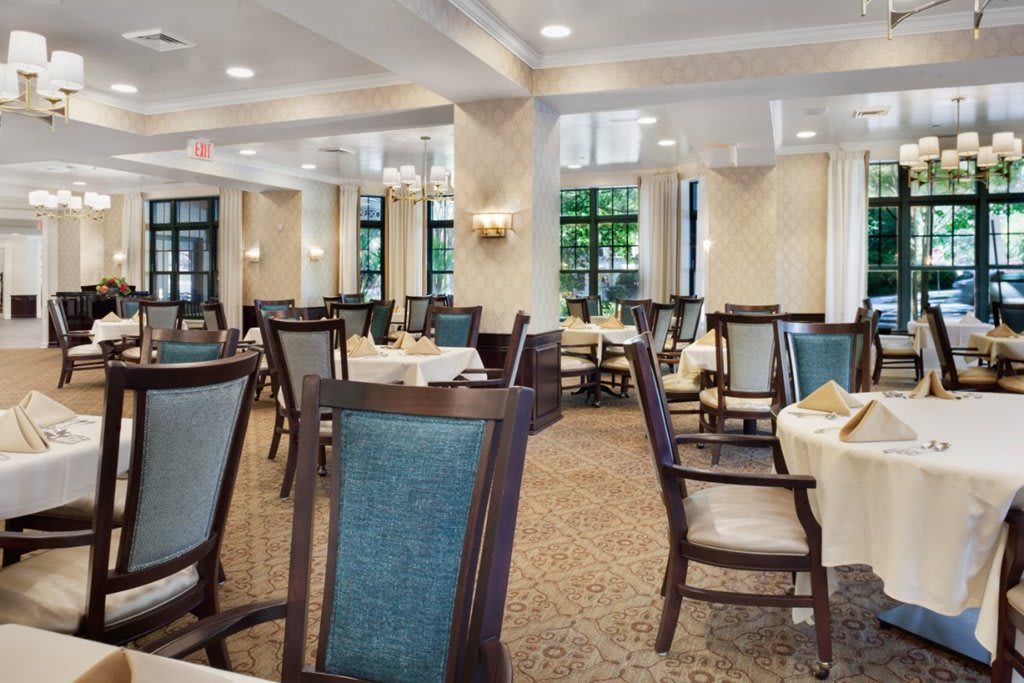 An elegant dining room with neatly arranged tables and chairs, softly lit by classic light fixtures.