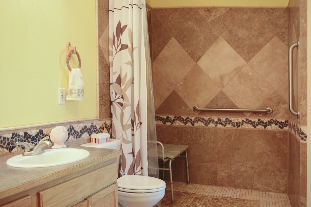 A tiled bathroom featuring a walk-in shower, floral curtain, sink, and accessible amenities.