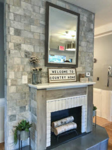 A rustic-style fireplace with a mirror above and a welcoming 'Country Home' sign.