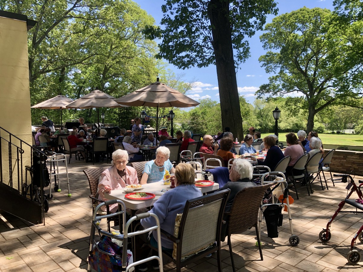 A group of seniors enjoying a meal at an outdoor restaurant surrounded by trees.