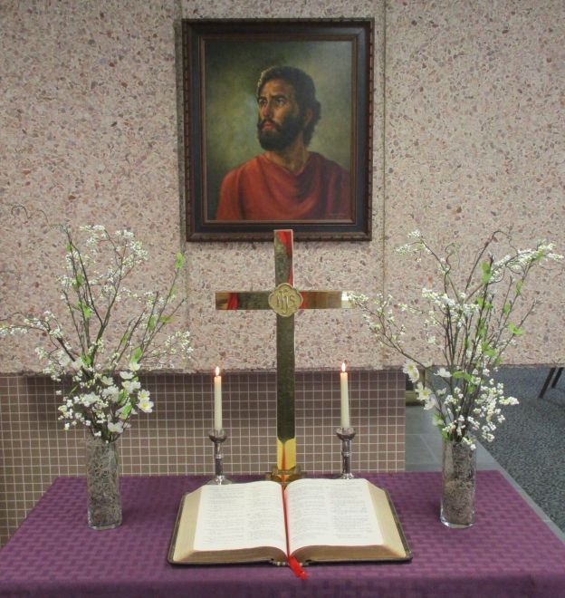 A Christian altar setup with a cross, open Bible, candles, and floral arrangements.
