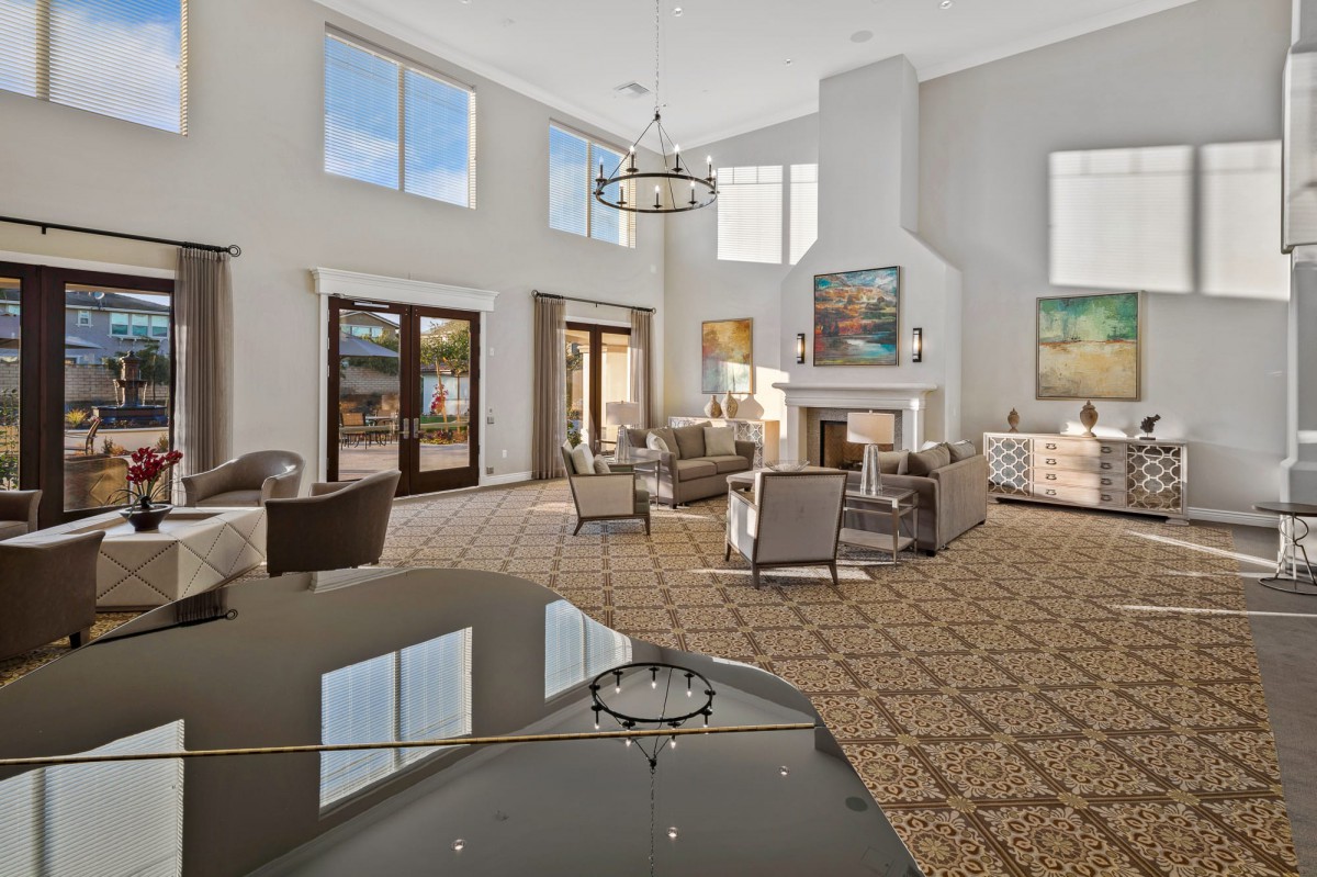 A spacious and modern living room with high ceilings, large windows, elegant chandeliers, and comfortable seating around a central fireplace.