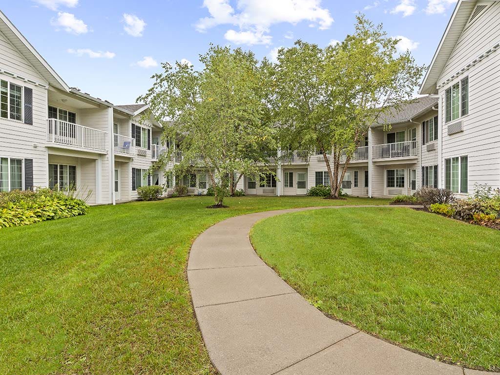 A serene courtyard surrounded by residential buildings with a winding pathway and lush greenery.