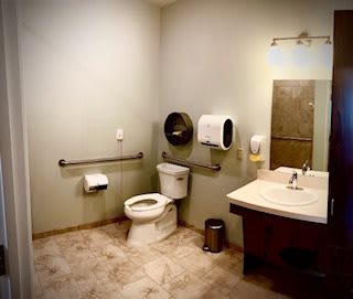 A clean and well-organized public restroom featuring a toilet, sink, and mirror.