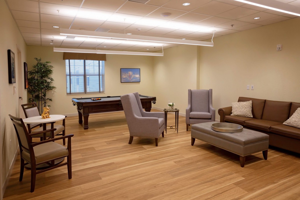 A modern lounge area featuring comfortable seating arrangements and a pool table, with wood flooring and neutral decor.