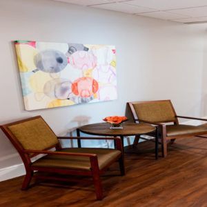 A modern waiting area with two chairs, a small table, and colorful artwork on the wall.