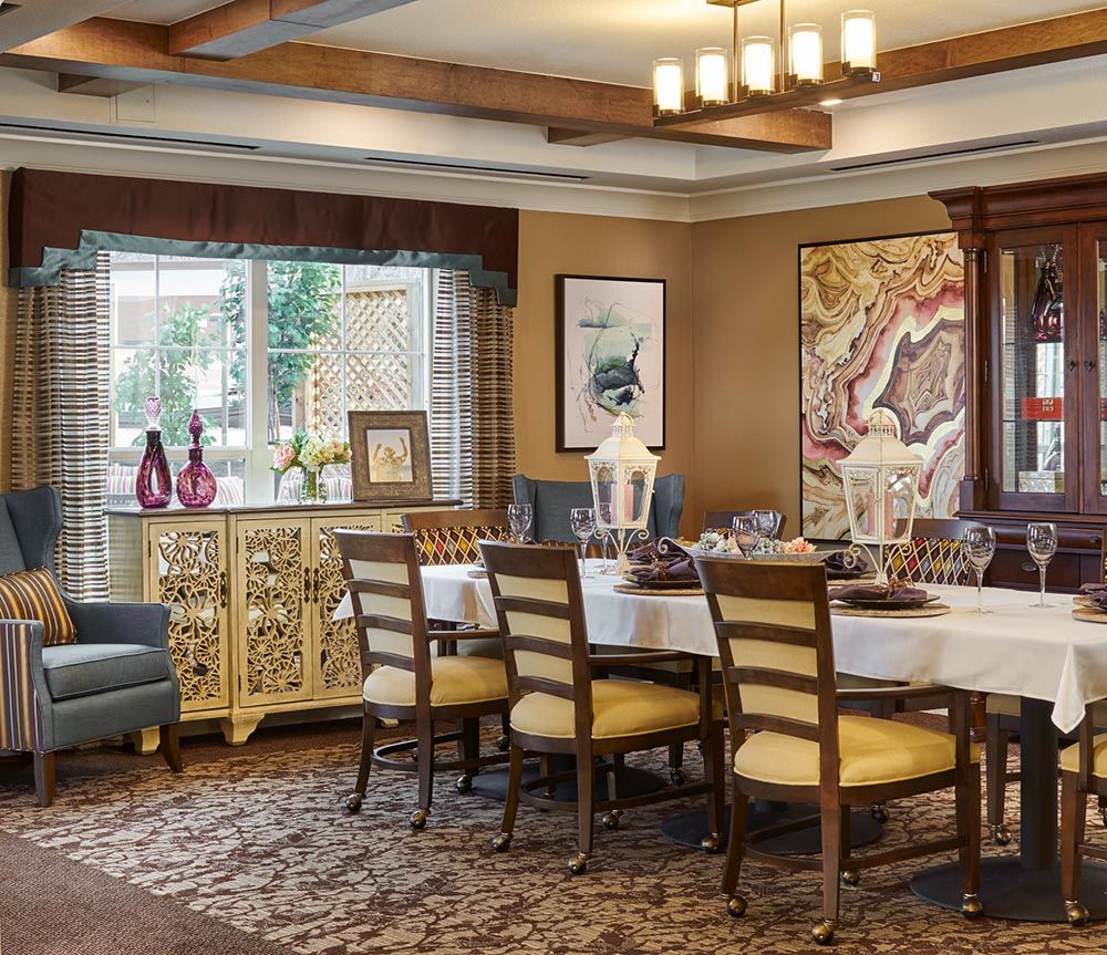 A warmly decorated dining room with a large table and chairs, featuring elegant artwork and a window view.