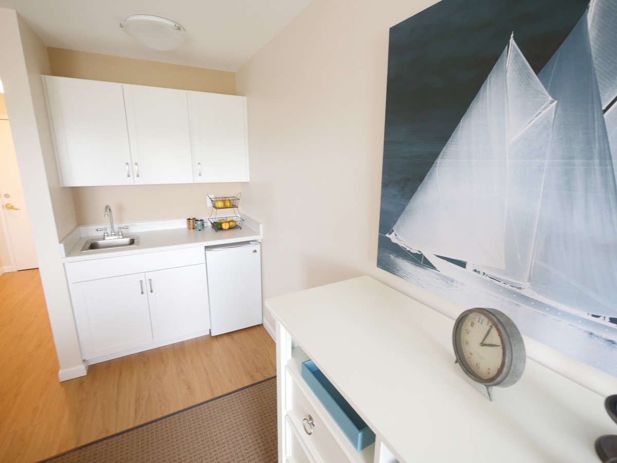 A minimalist kitchen with white cabinets and a sailboat painting on the wall.