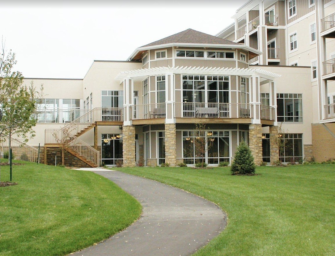 A modern building with large windows and a pathway leading up to it, surrounded by a well-maintained lawn.