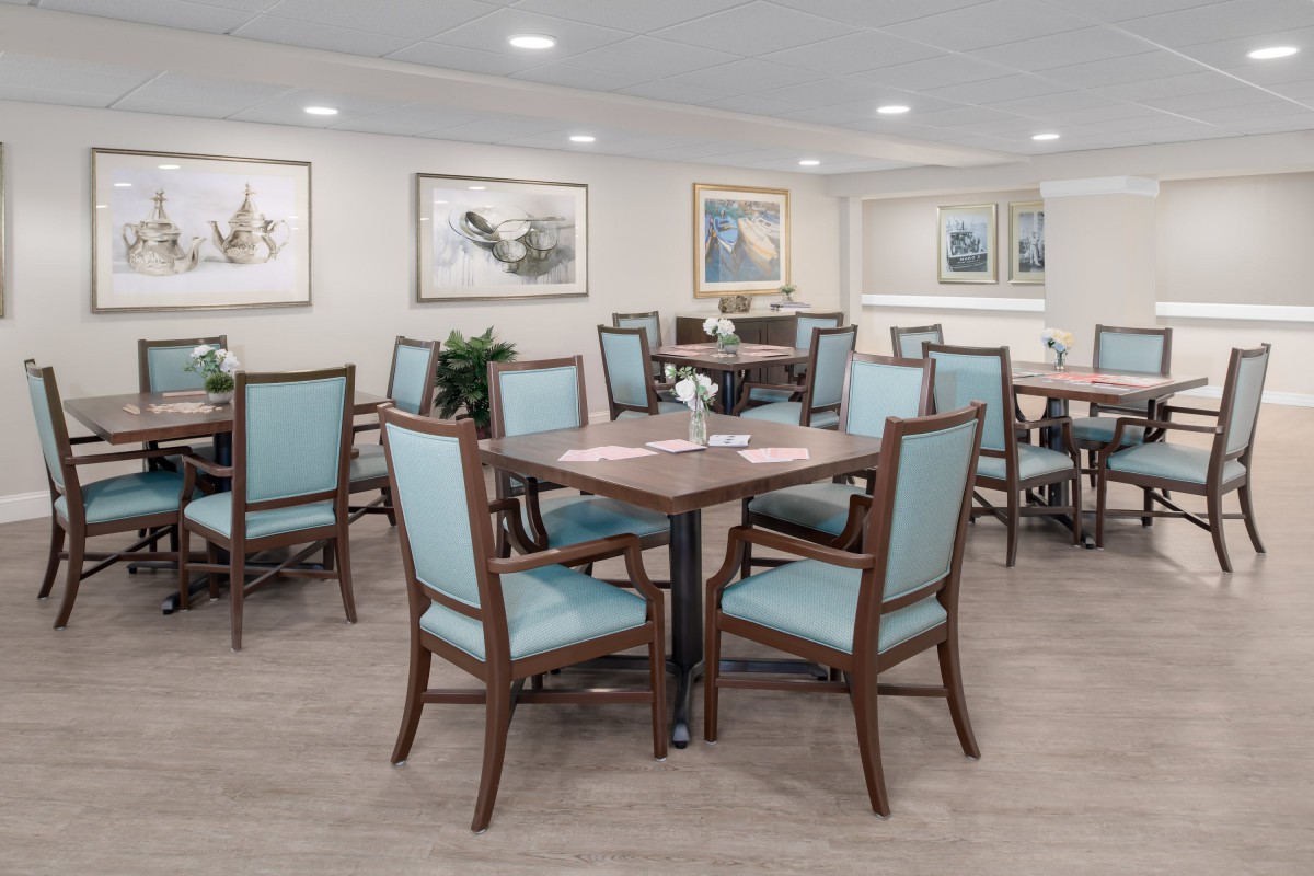 A modern dining room with neatly arranged tables and chairs, decorated with paintings on the walls.