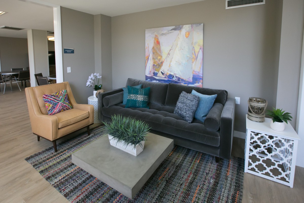 A modern living room featuring a grey sofa, an armchair, a coffee table with a plant centerpiece, and abstract artwork on the wall.