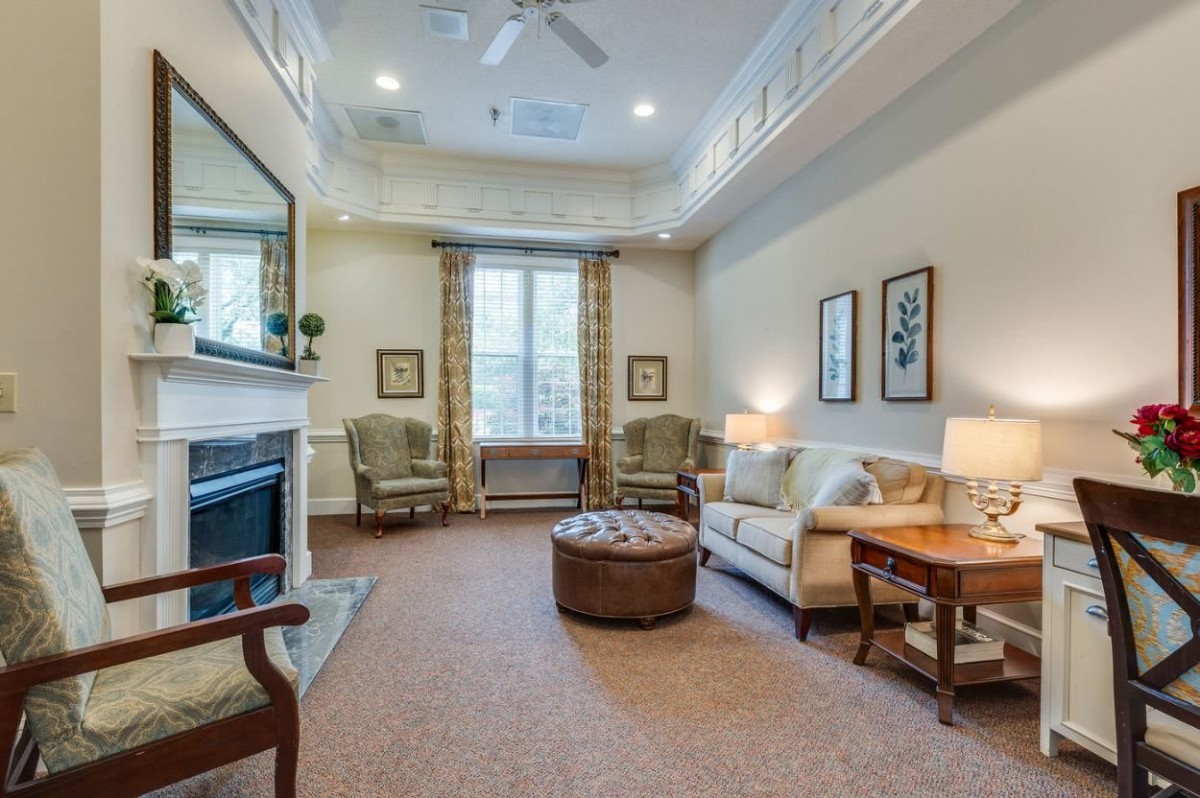 A cozy living room with a sofa, armchairs, a coffee table, and a fireplace, beautifully accented with decorative art and large windows.