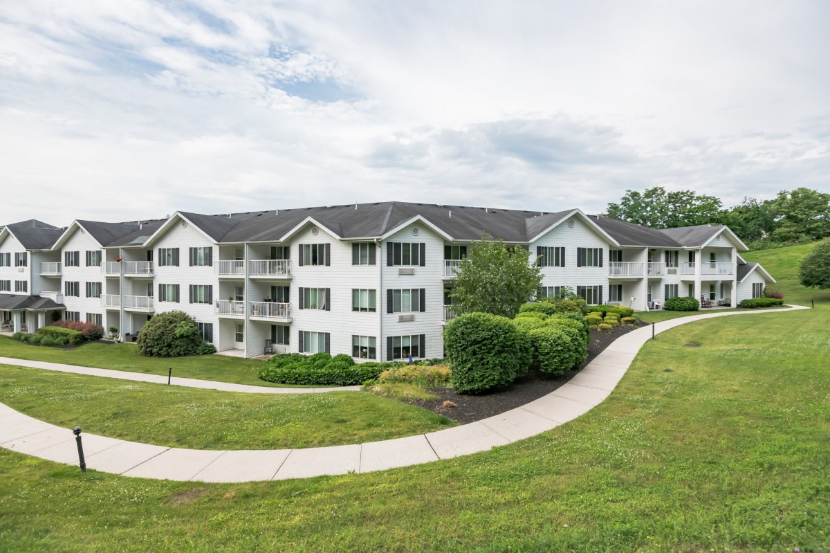 A three-story apartment building surrounded by neatly landscaped lawns and winding pathways.