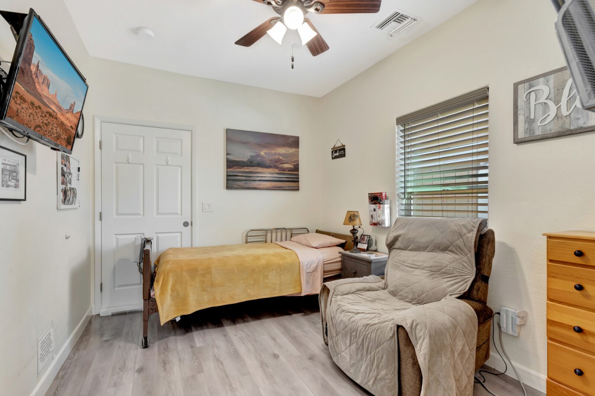A cozy bedroom featuring a single bed, an armchair, and a ceiling fan.
