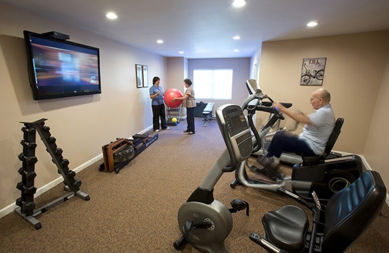 A fitness room with exercise equipment including a stationary bike, where people are engaged in their workout.