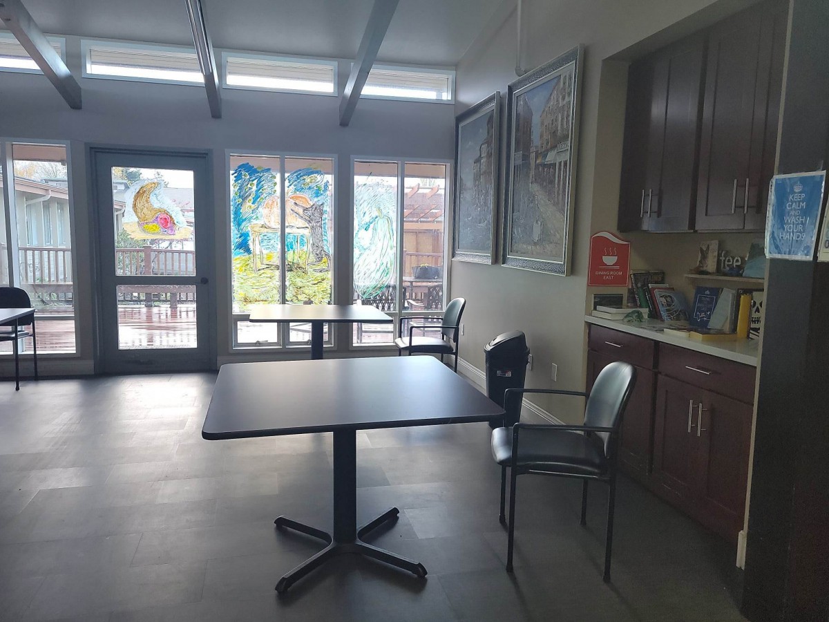A bright cafeteria space with tables and chairs, decorated with colorful artwork on the windows.