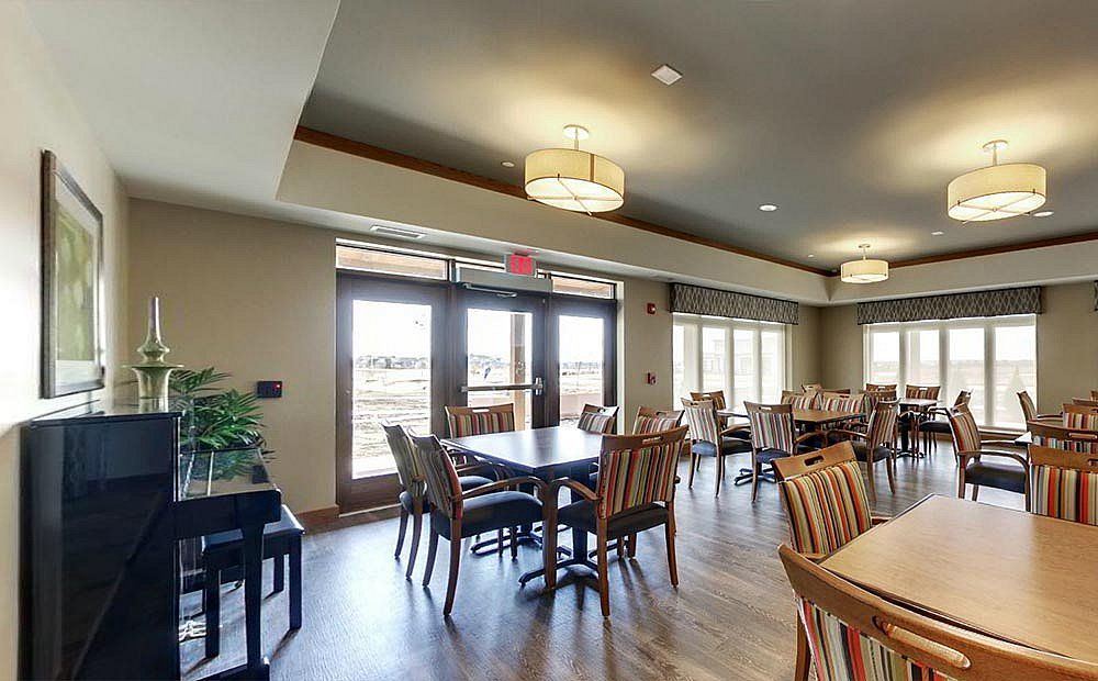A spacious dining area with wooden tables and chairs, featuring large windows and modern lighting.