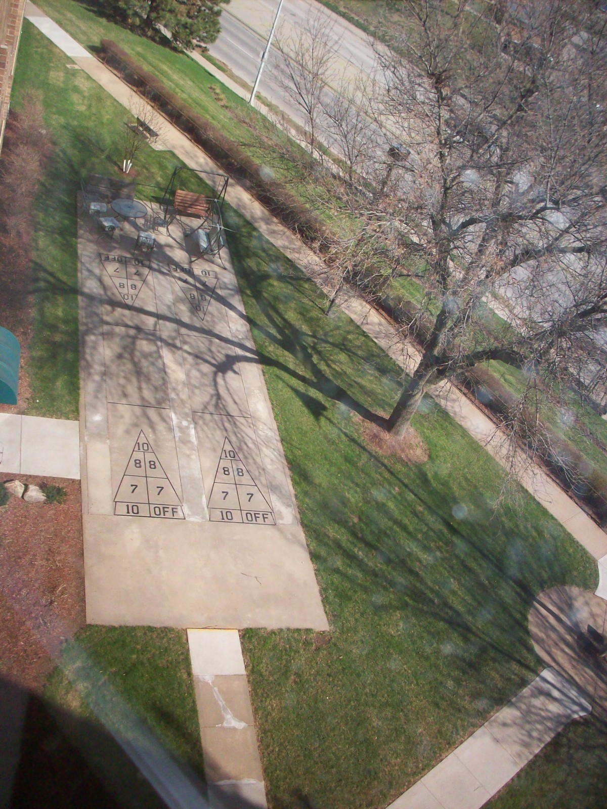 Aerial view of a concrete path and tree casting shadows on a grassy area.