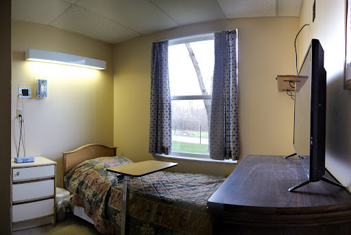 A cozy hospital room featuring a bed, table, and window with natural light.