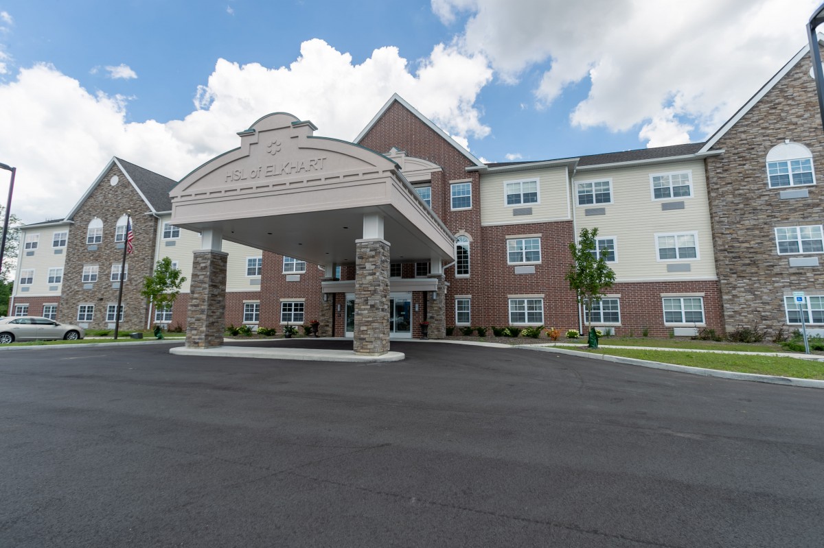 A three-story hotel with a covered entrance and brick facade under a partly cloudy sky.