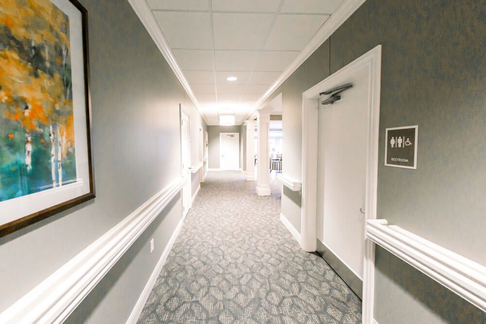 A long hallway with a patterned carpet, lined with doors and softly lit by ceiling lights.