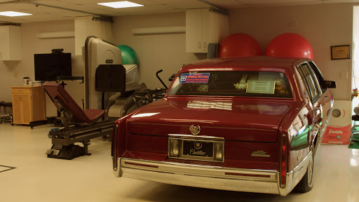 A red car parked in a garage alongside exercise equipment and fitness balls.