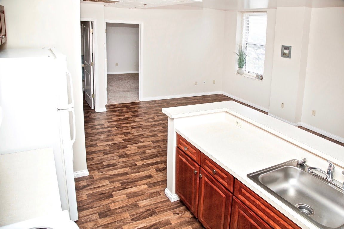 A modern apartment kitchen with wood flooring and sleek cabinetry.