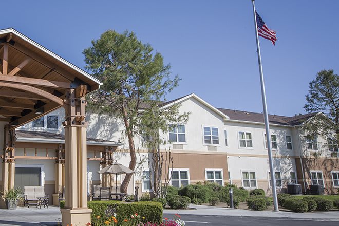 A two-story building with a flagpole and tree in front, set against a clear blue sky.