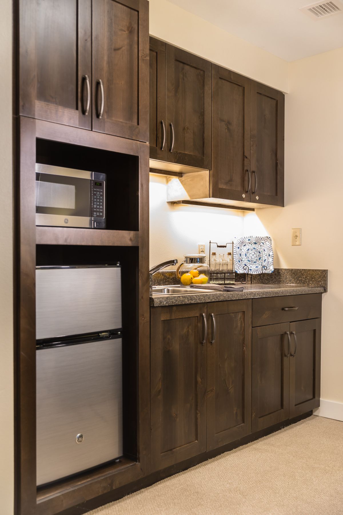 A compact kitchen with wooden cabinets, a microwave, and a small refrigerator.