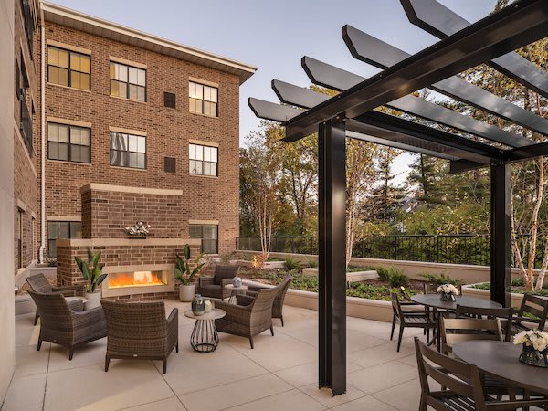 A cozy apartment patio featuring comfortable outdoor seating, a modern fireplace, and a stylish pergola.
