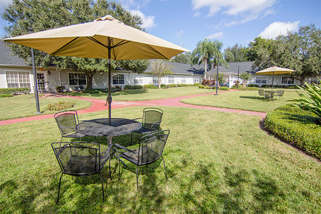 A sunny outdoor patio with tables and chairs under large umbrellas set in a grassy garden area.