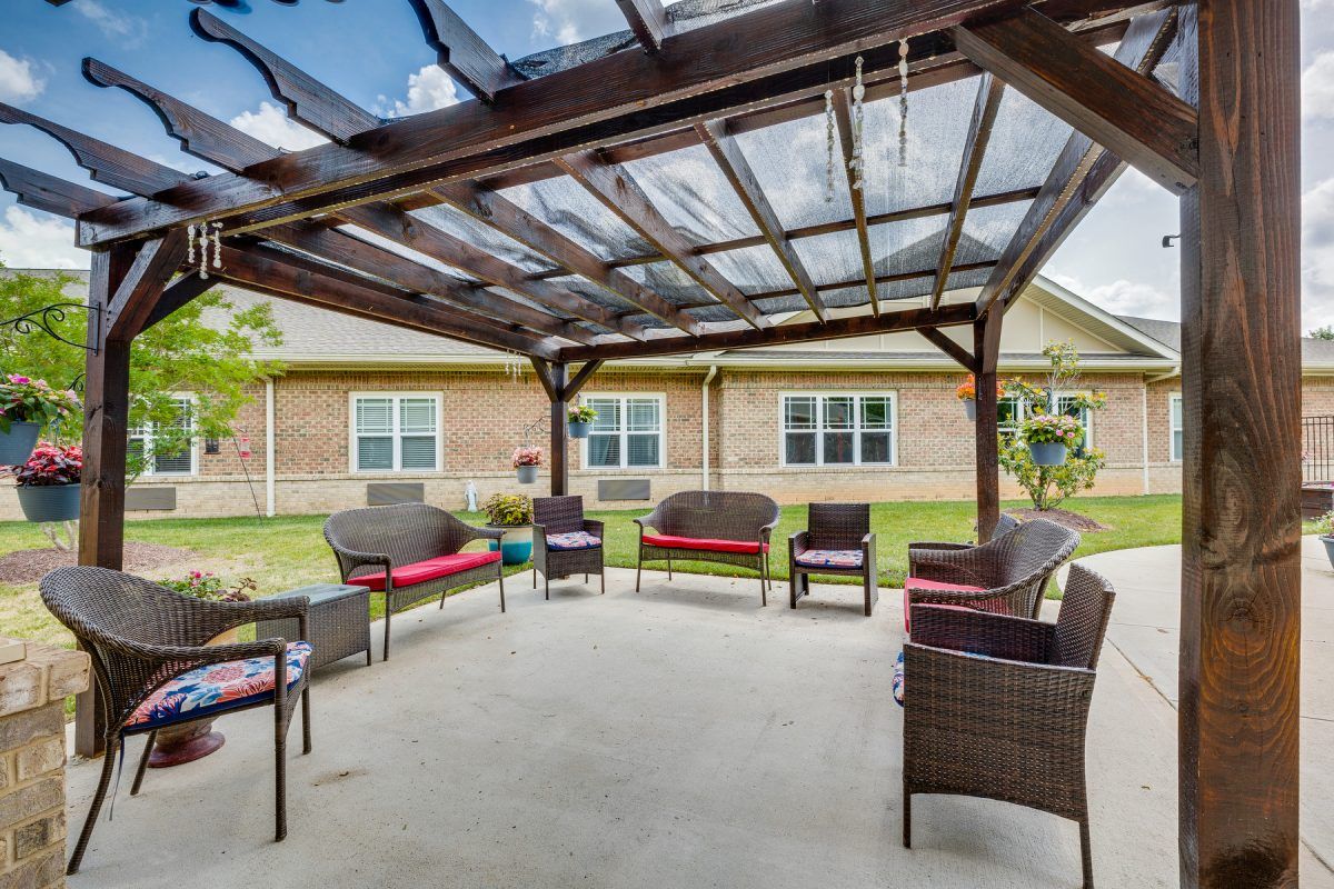 A well-furnished backyard patio with a pergola, featuring wicker furniture and a garden view.