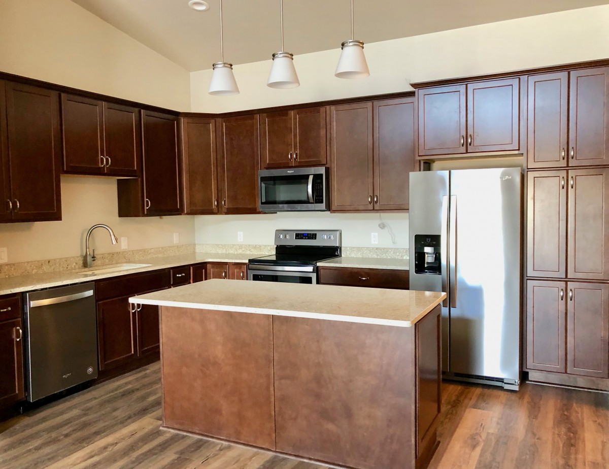 A modern kitchen with brown cabinets, stainless steel appliances, and a central island.
