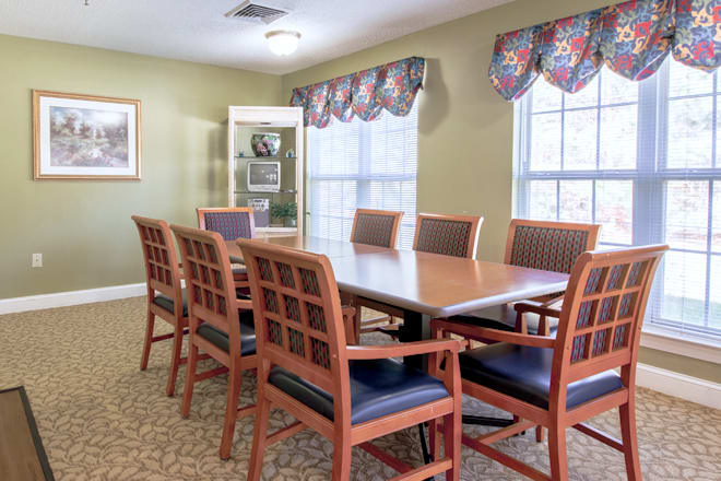A well-lit conference room with a long meeting table surrounded by wooden chairs and two large windows.
