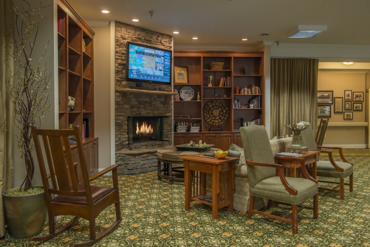 A cozy living room with a fireplace and bookshelves, featuring comfortable furniture and a TV mounted above the hearth.