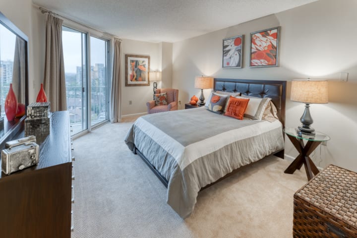 A modern bedroom with stylish decor, featuring a large bed, artwork on the walls, and a city view through the window.
