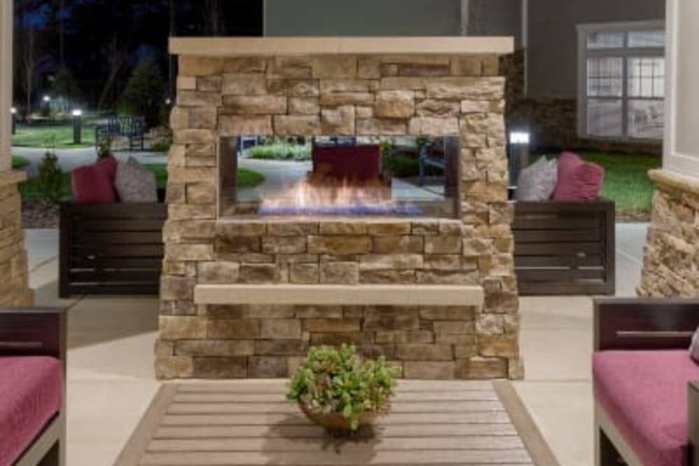 A cozy outdoor stone fireplace on a patio, surrounded by comfortable seating and a potted plant.