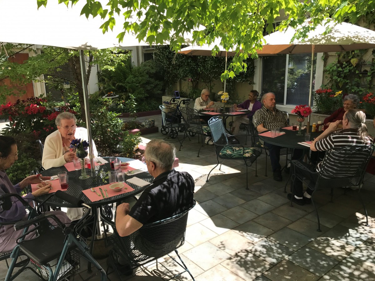 A group of people enjoying their meals at an outdoor restaurant patio under sun umbrellas.