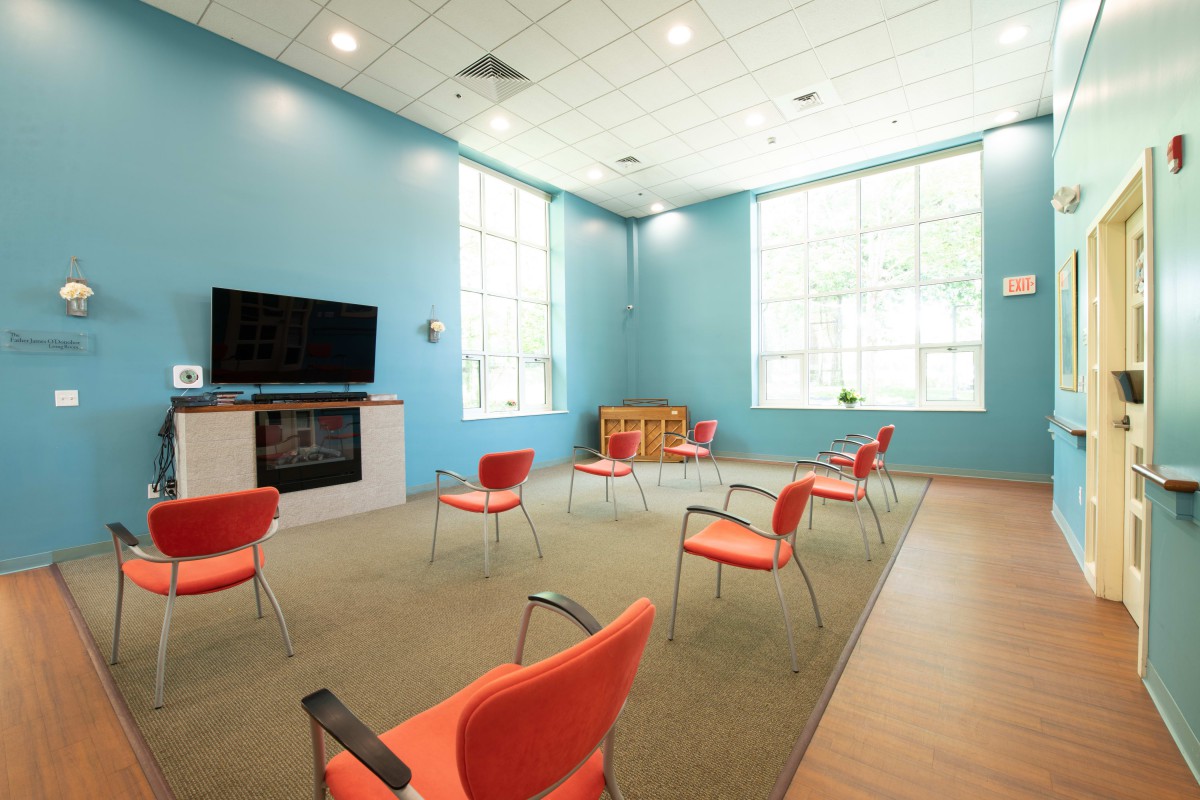 A bright and spacious meeting room with red chairs arranged in a circle, featuring a television and a children's play area.