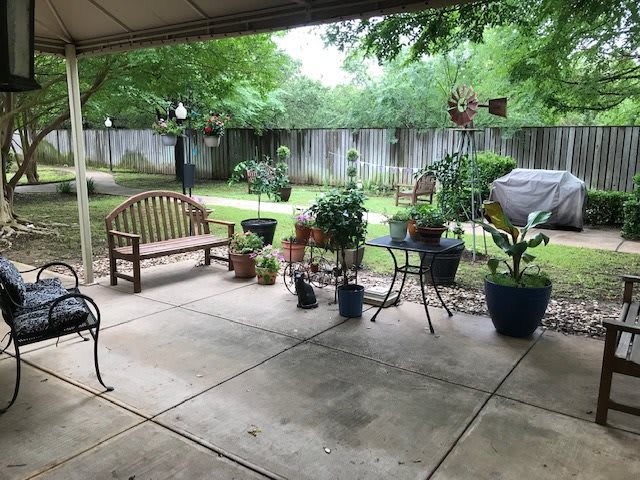 A cozy backyard patio with benches and various potted plants under a covered area.