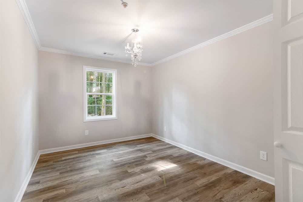 A minimalist empty room with hardwood flooring and natural light from a window.