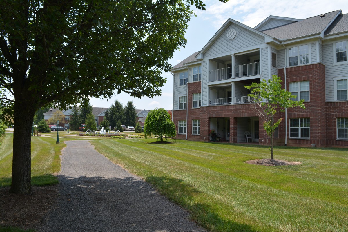 A sunny day view of a residential apartment building with a paved pathway and well-kept grass.
