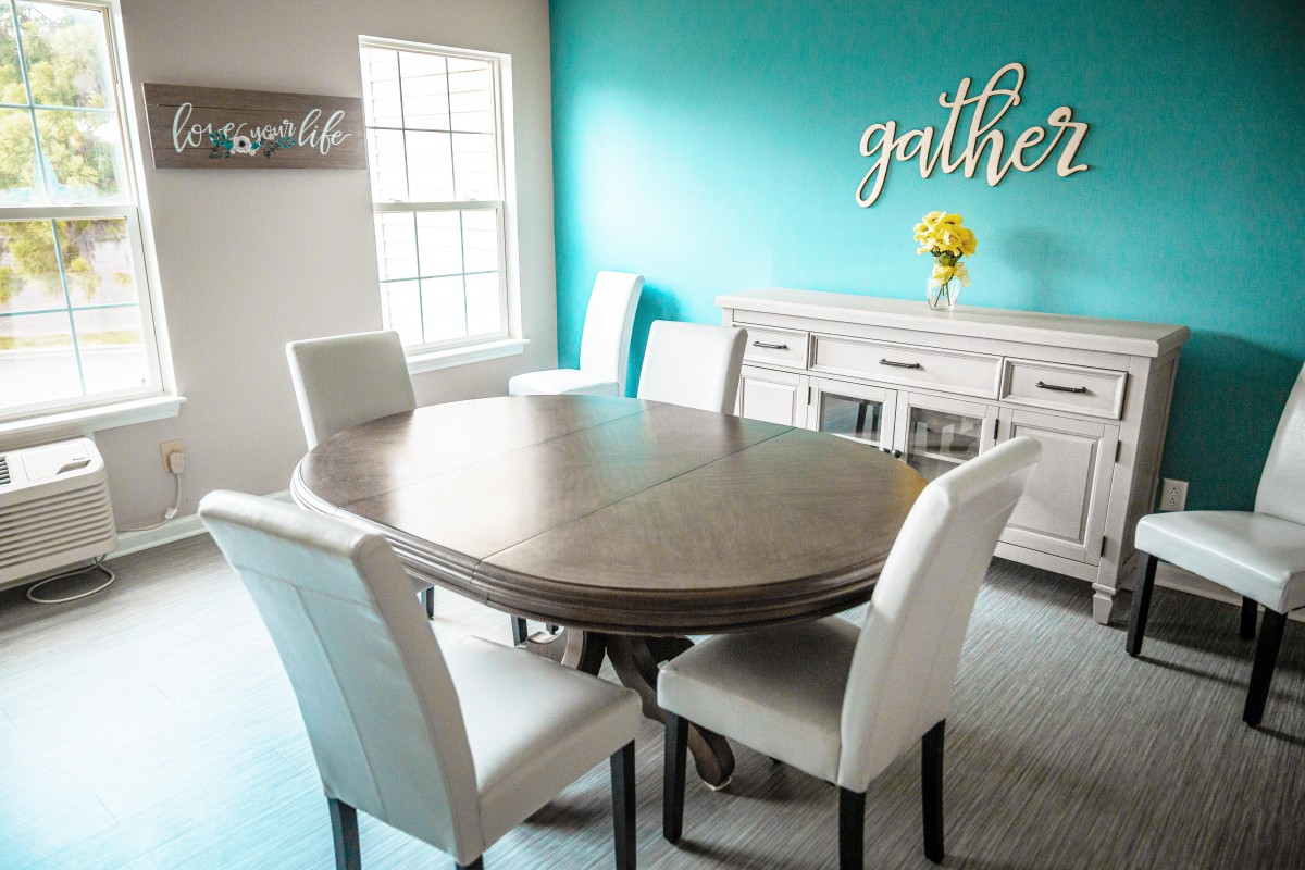 A modern dining room with a wooden table and white chairs, featuring a bright turquoise accent wall.