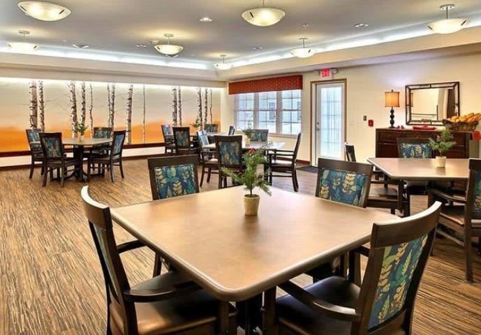 A spacious dining room with multiple tables and chairs, featuring warm lighting and a comfortable atmosphere.