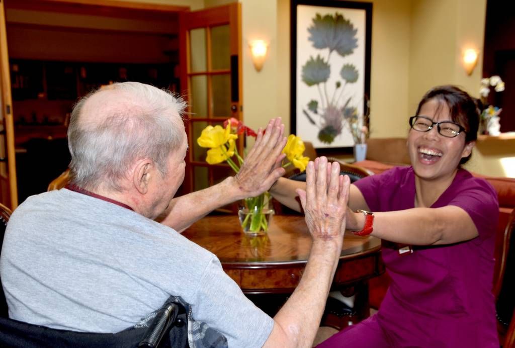 A joyful interaction between a caregiver and an elderly person in a nursing home setting.