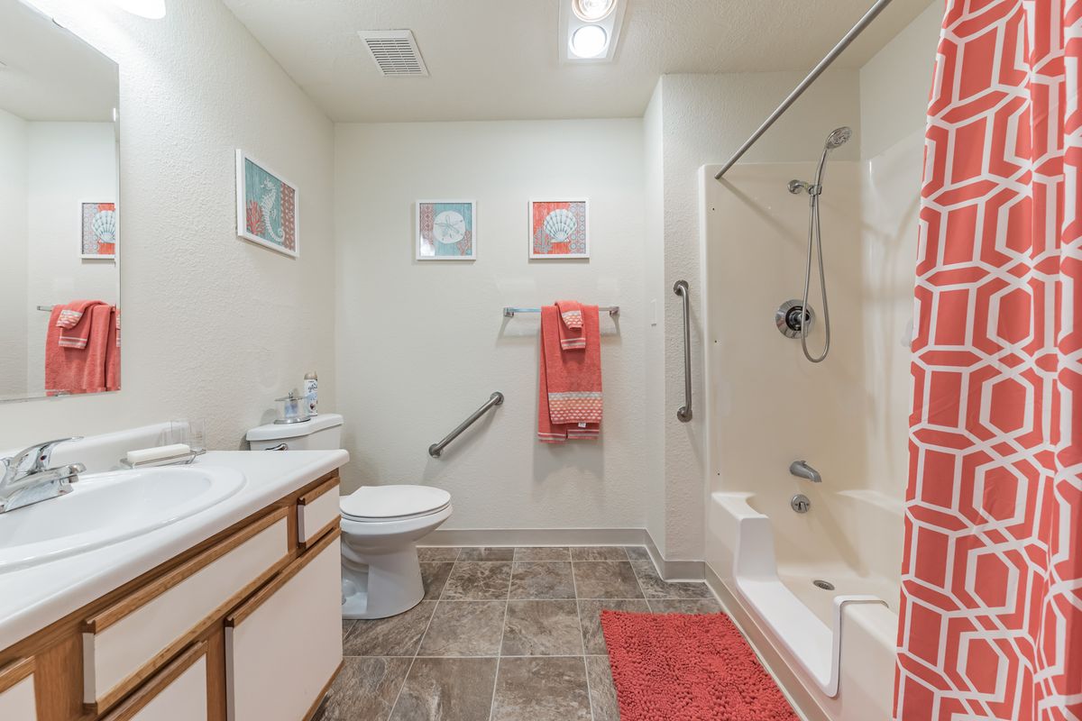 A modern bathroom with a shower, toilet, and sink, decorated with red accents and wall art.
