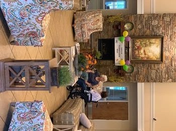 A warm living room setting with people gathered for a celebration, featuring colorful balloons and a banner above the fireplace.