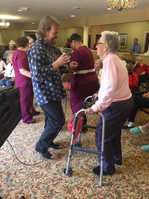 An elderly person with a walker enjoys dancing with others in a community setting.