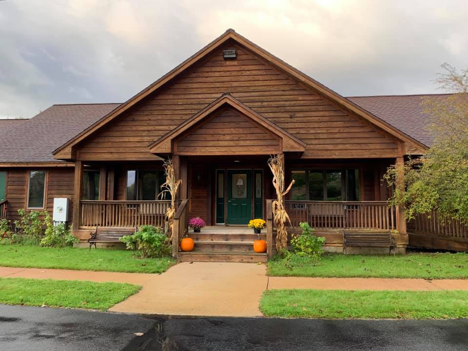 A cozy wooden house with autumn decorations on the porch, including pumpkins and flowers.