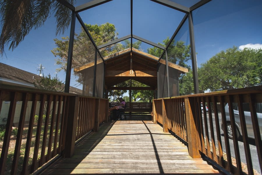 A wooden gazebo with a pathway leading towards it, surrounded by trees on a sunny day.